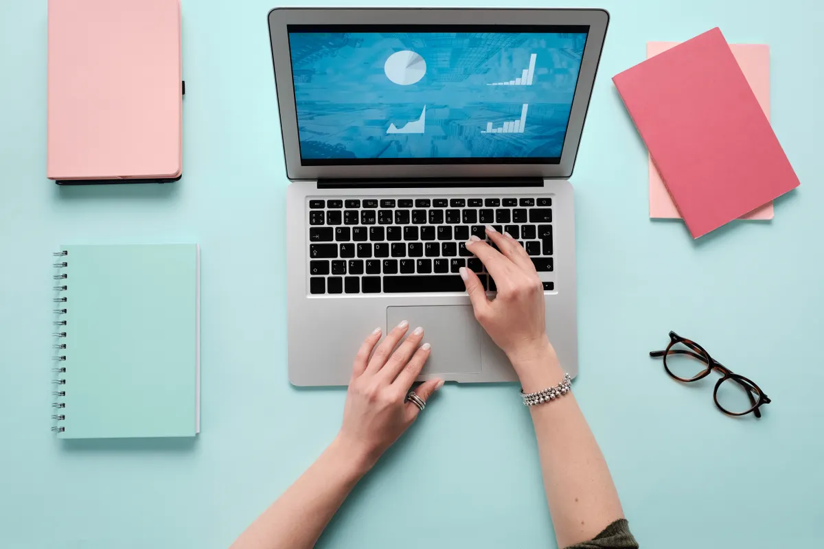 Hands typing on a laptop that shows simple charts, on a teal desk